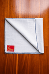 Light grey woolen pooja mat folded with blue stitched border and red label patch.
