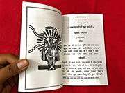 Open religious book with line-drawn figure and Hindi text on cream pages