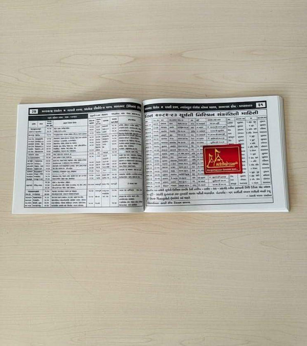 Open Gujarati panchang book with printed tables and red logo on right page.