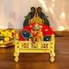 Gold-plated brass singhasan with peacock-style back and seated deity figure on red cushion.