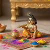 Golden pichkari and matki set beside painted Krishna idol on decorated cloth