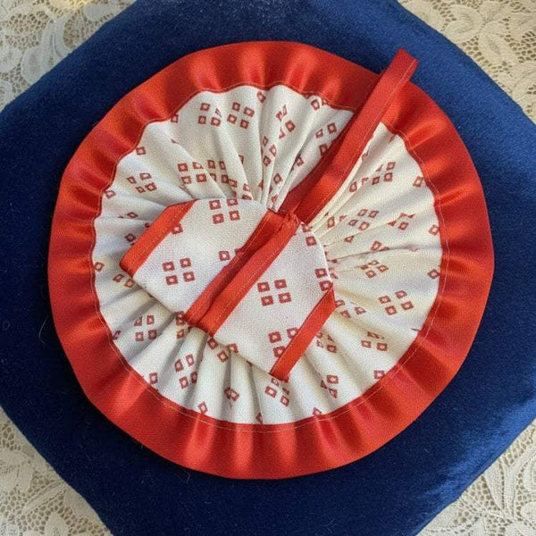 Krishna dress rosette close-up with red satin trim, white patterned fabric, blue backing