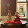 Wooden deity figurines set, two seated dolls on round base, gold and red patterned dresses.