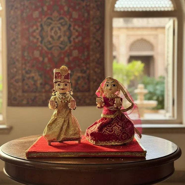Wooden deity figurines set, two seated dolls on round base, gold and red patterned dresses.