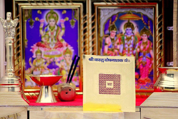 Gold yantra card with black square mandala and Devanagari text on a platform