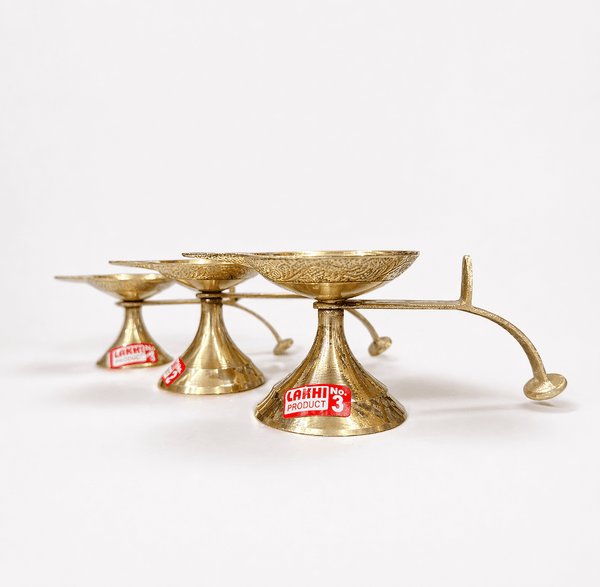 Brass aarti diya stand set with handle, three shallow oil cups on pedestal bases.