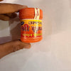 Orange chandan tika jar with ribbed lid and printed label, held in hands.
