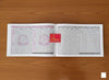 Panchang calendar book with open pages of date tables and red emblem label