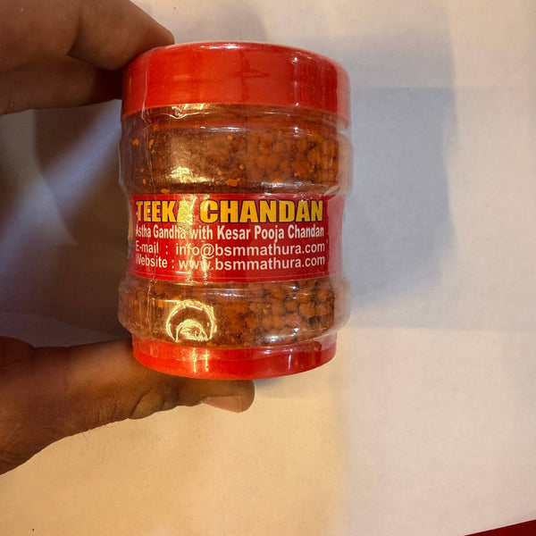 Chandan powder jar with red lid and spice contents, shown in hand.